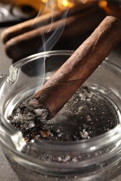Smoldering cigar in ashtray on grey table, closeup