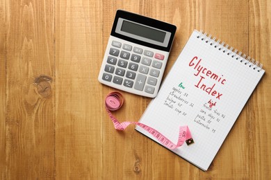 Photo of List with products of low and high glycemic index in notebook, calculator and measuring tape on wooden table, flat lay. Space for text