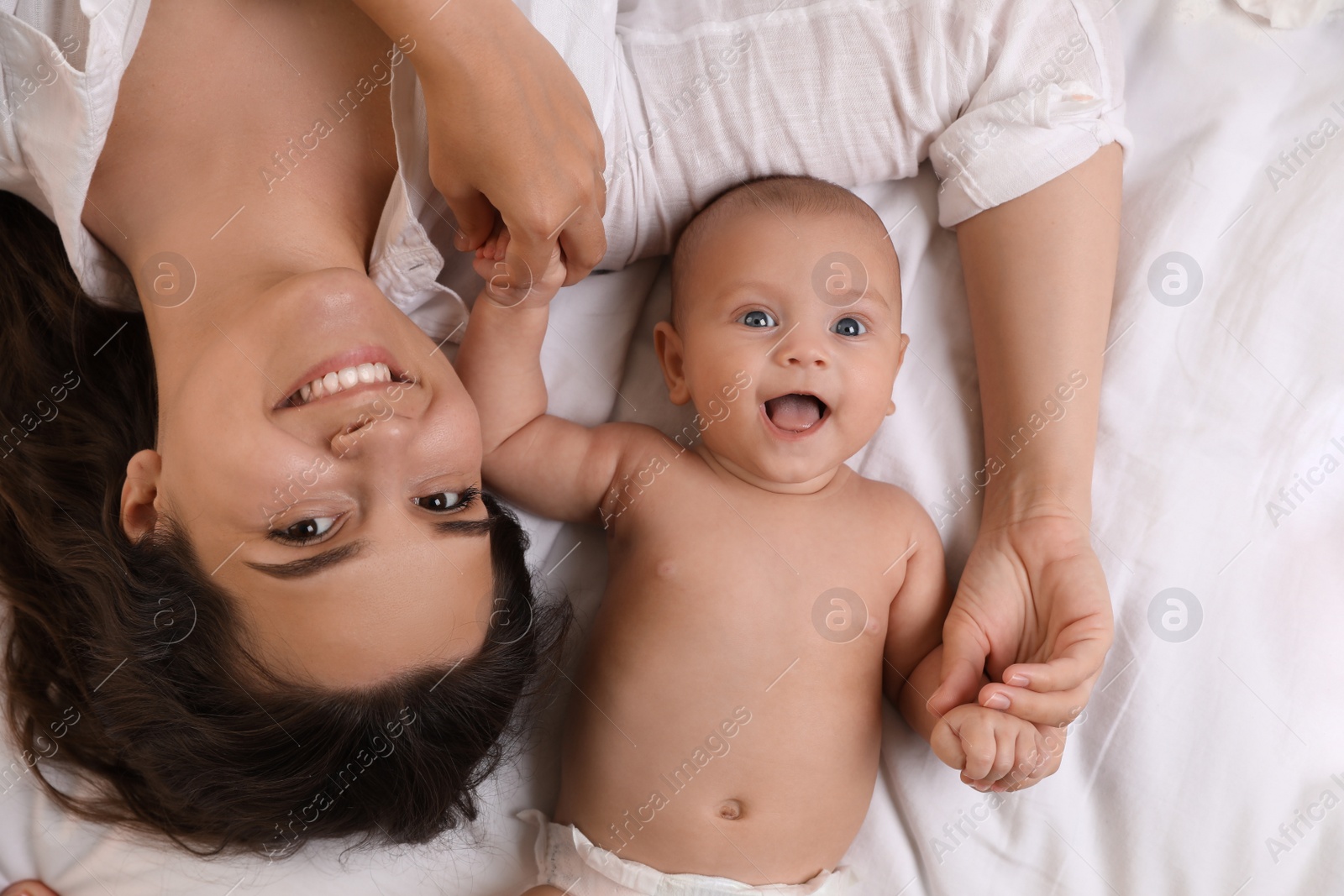 Photo of Happy young mother with her cute baby on bed, top view