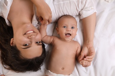 Happy young mother with her cute baby on bed, top view