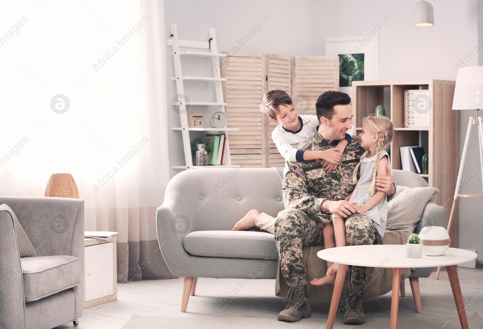 Photo of Young man in military uniform with his children on sofa at home