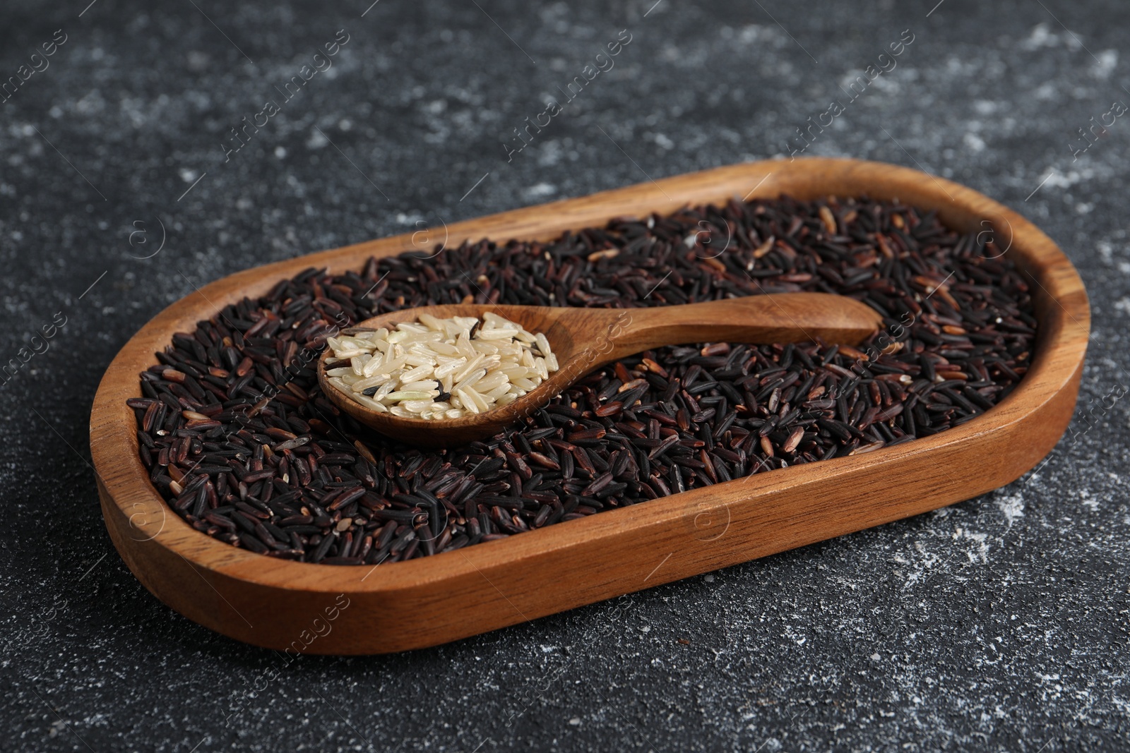 Photo of Spoon and dish with different sorts of rice on black textured table, closeup