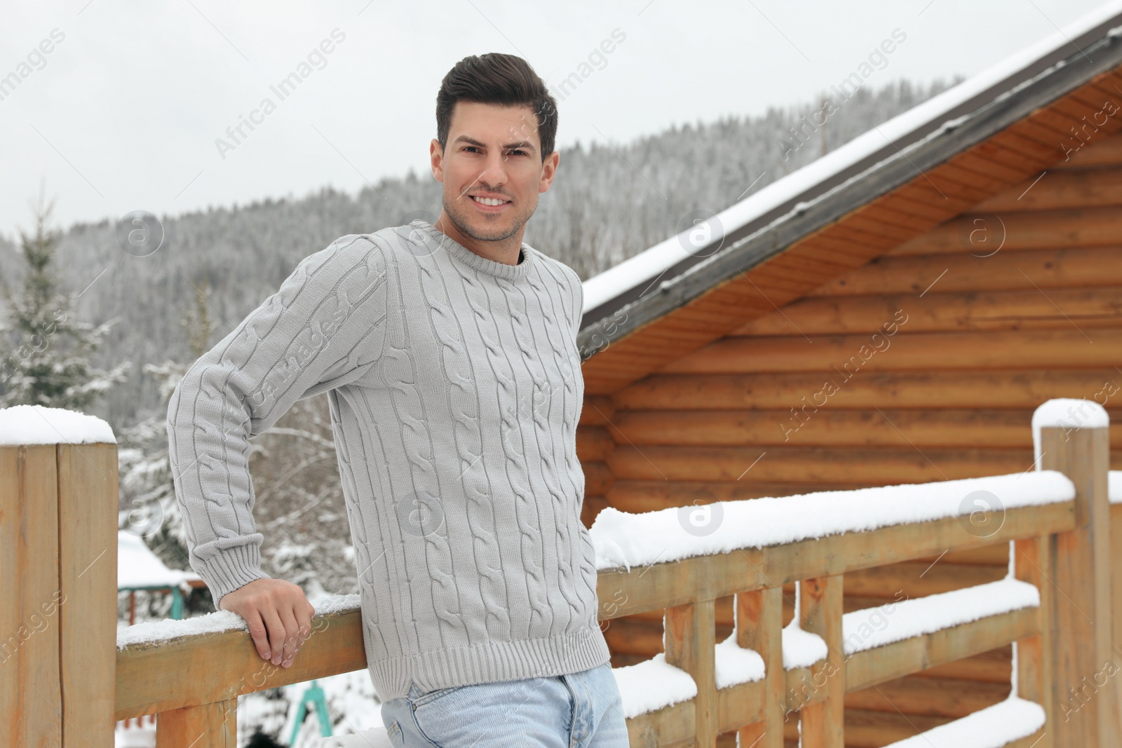 Photo of Happy man in warm sweater near wooden railing outdoors