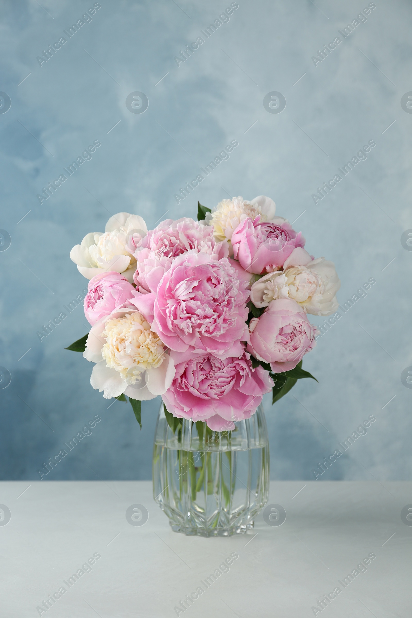 Photo of Bouquet of beautiful peonies in glass vase on white table