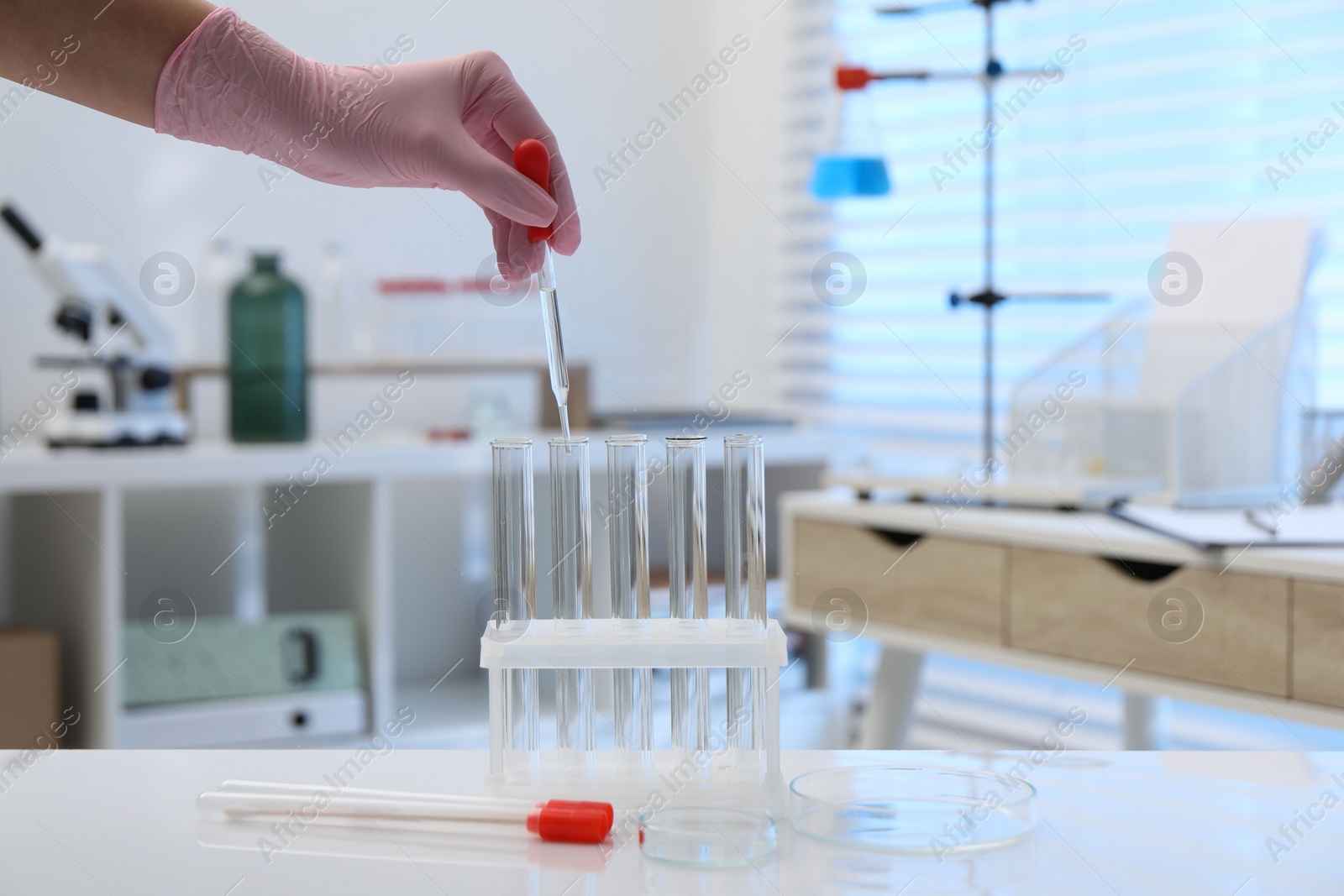 Photo of Laboratory analysis. Woman dripping liquid into test tubes at white table indoors, closeup