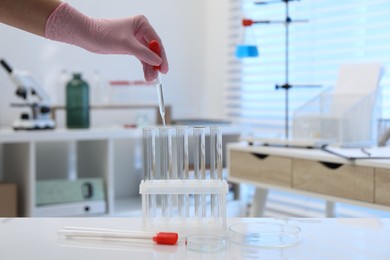 Laboratory analysis. Woman dripping liquid into test tubes at white table indoors, closeup