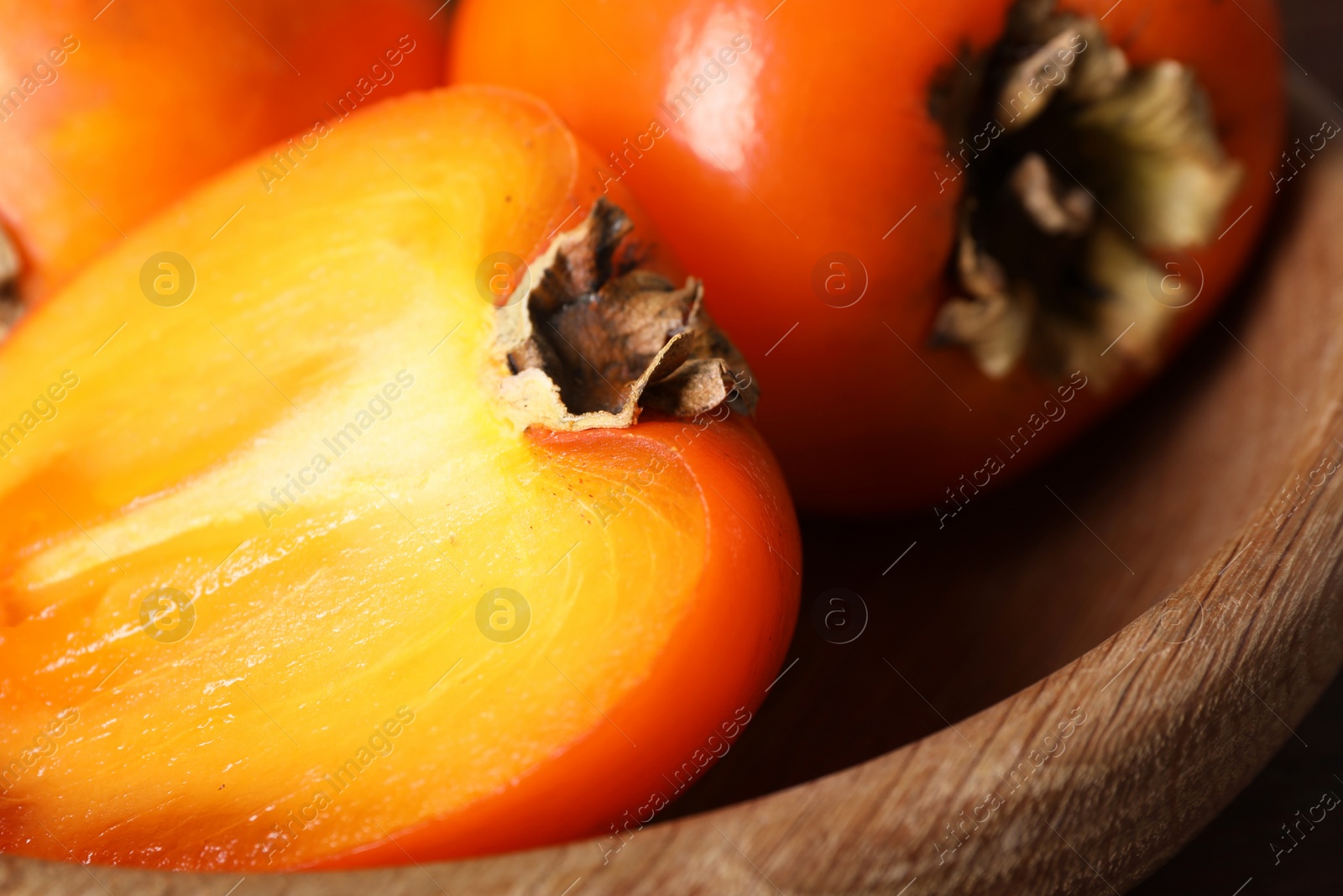 Photo of Delicious ripe persimmons in wooden bowl, closeup