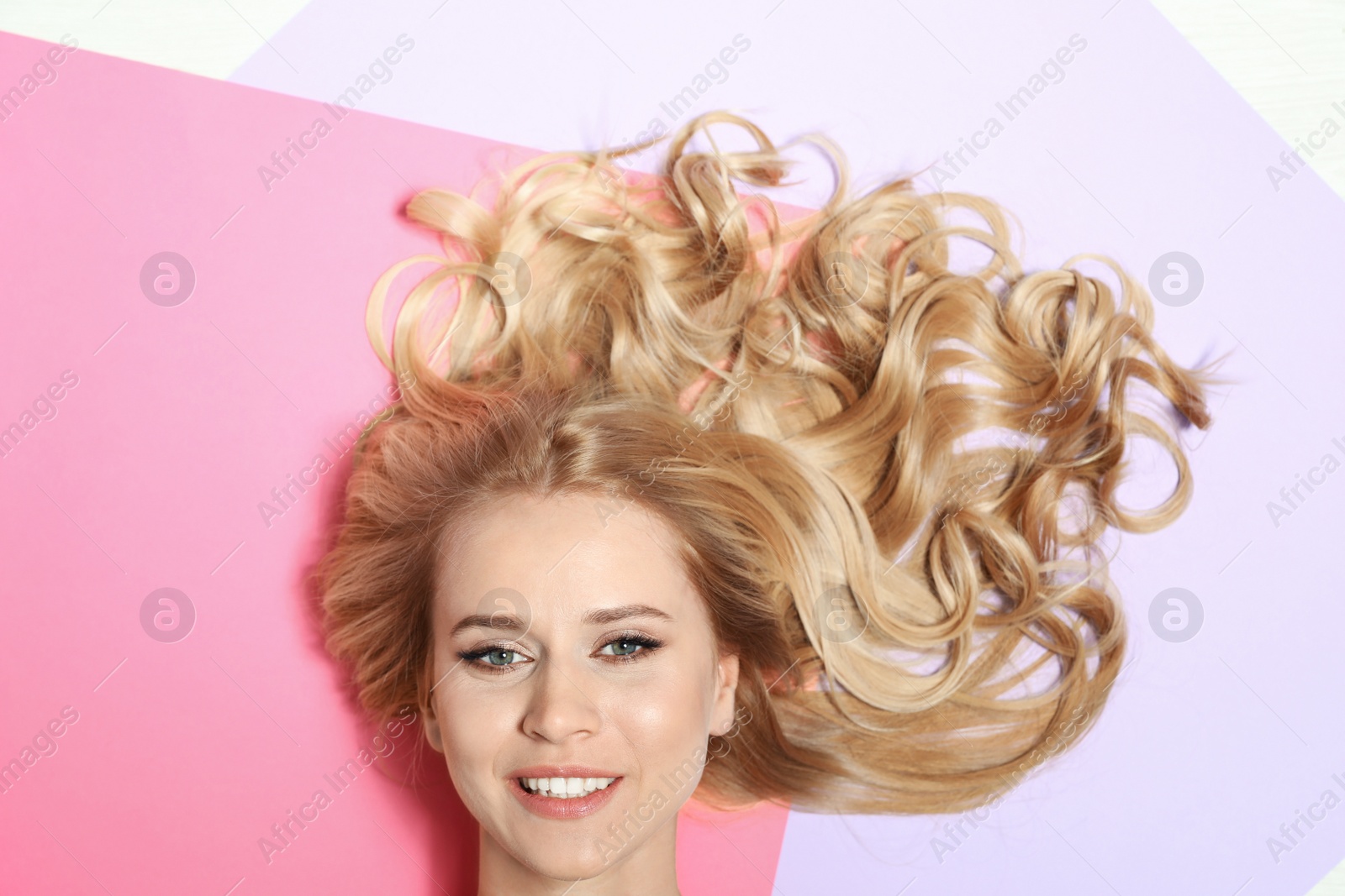 Photo of Beautiful woman with healthy long blonde hair on color background, top view