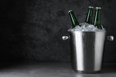 Photo of Metal bucket with beer and ice cubes on grey table. Space for text