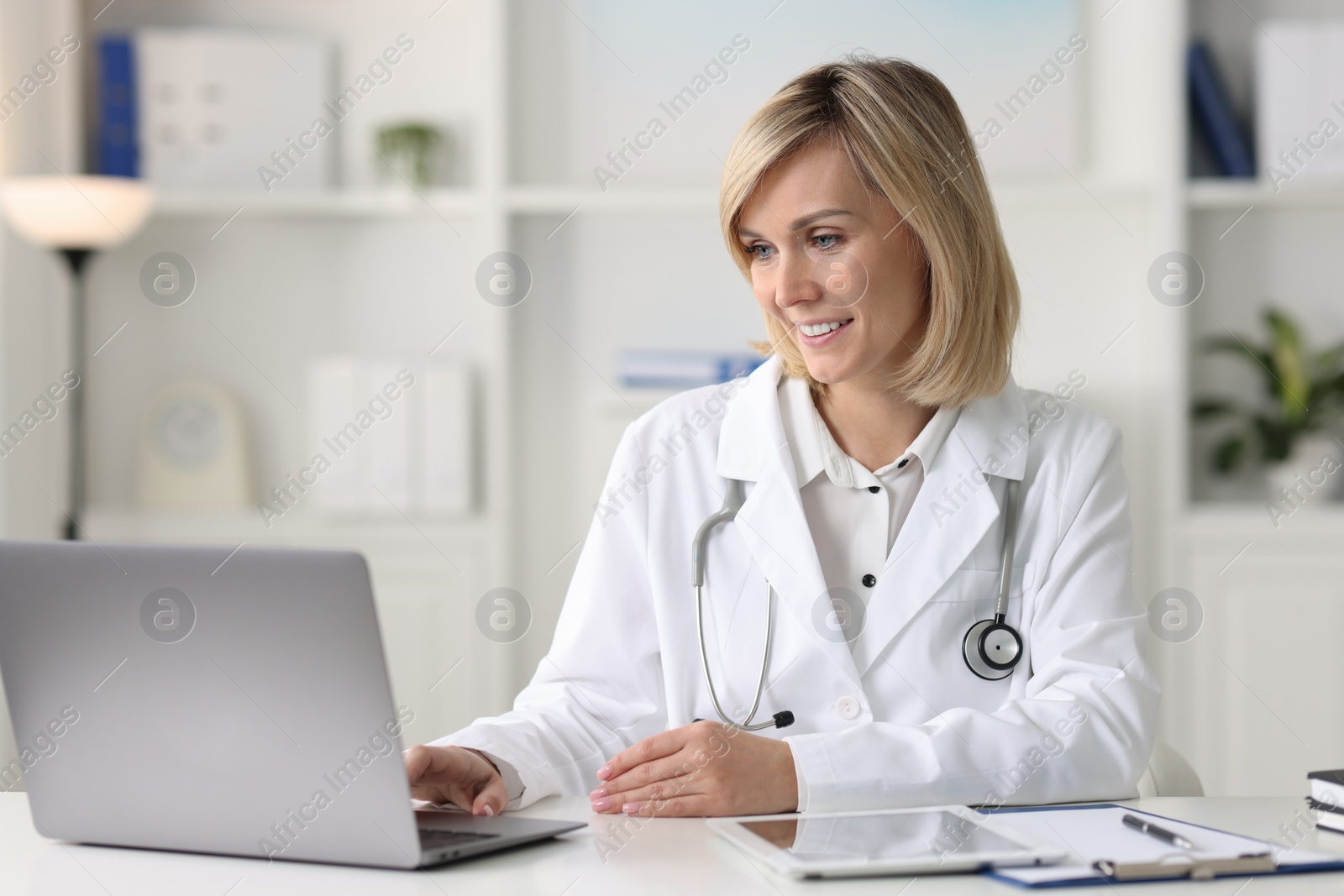 Photo of Smiling doctor with laptop having online consultation at table in office