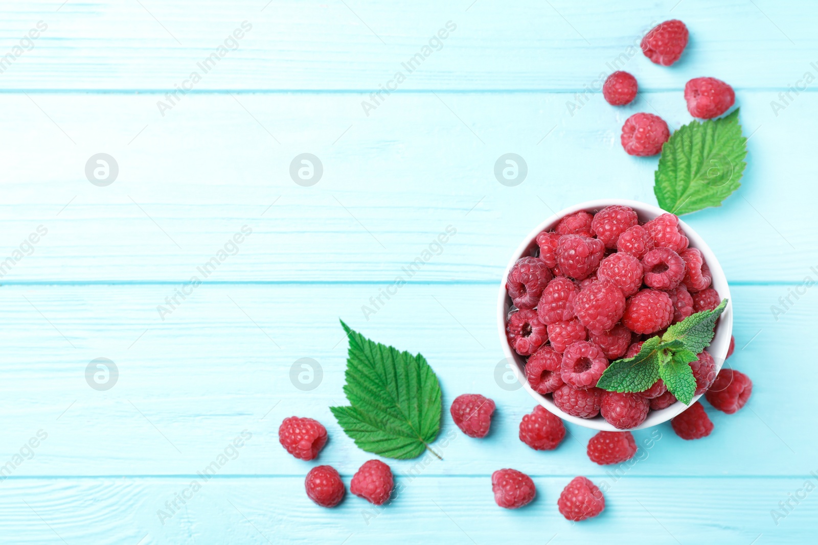 Photo of Bowl with ripe aromatic raspberries on wooden table, top view