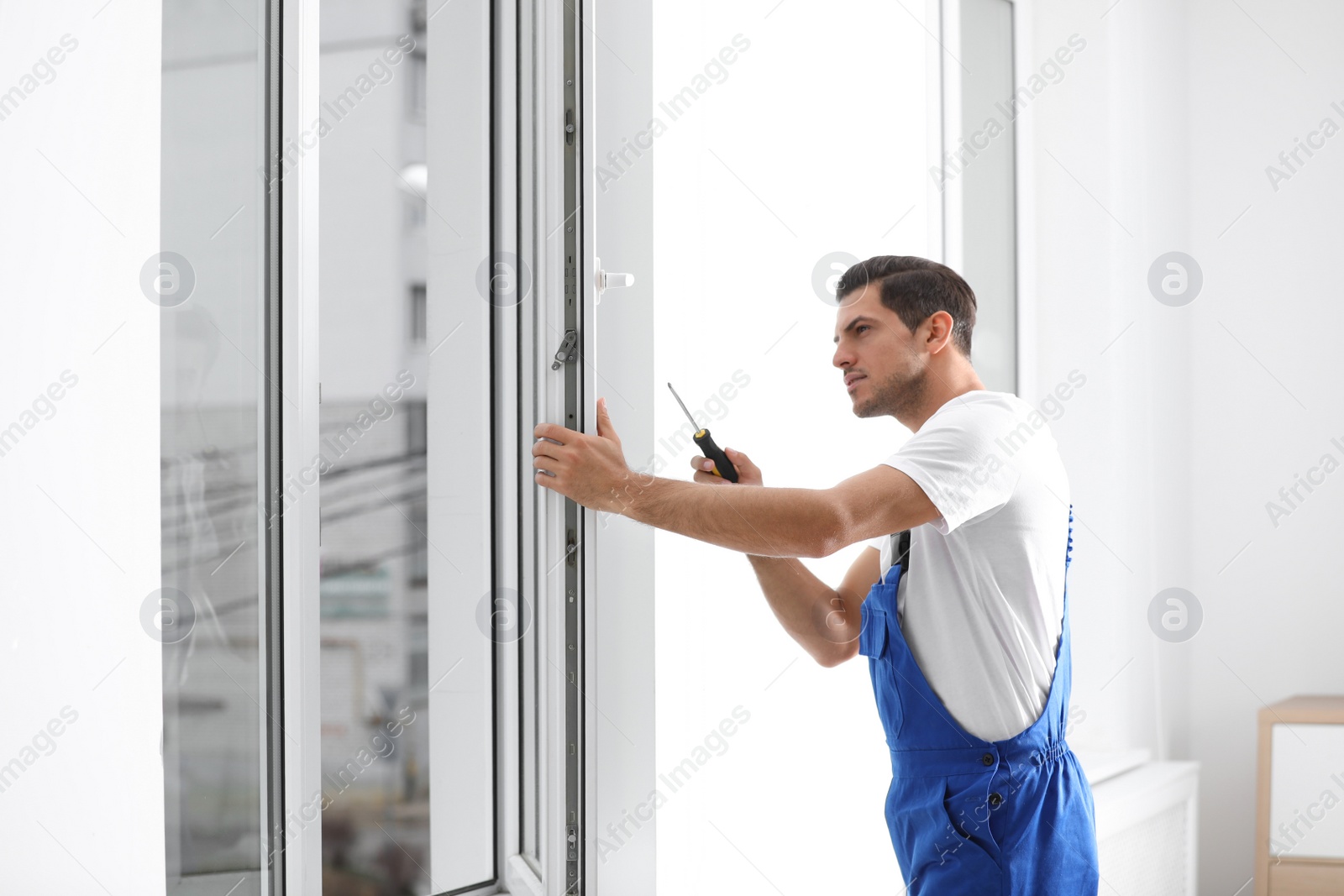 Photo of Construction worker repairing plastic window with screwdriver indoors