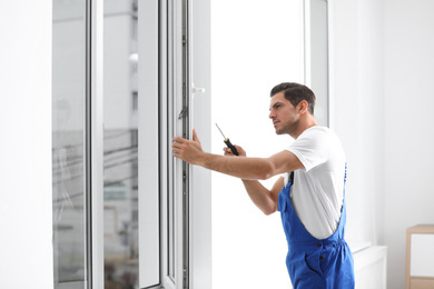 Construction worker repairing plastic window with screwdriver indoors