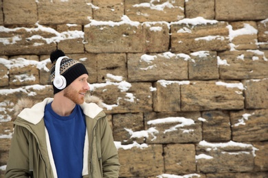 Photo of Young man listening to music with headphones against stone wall. Space for text
