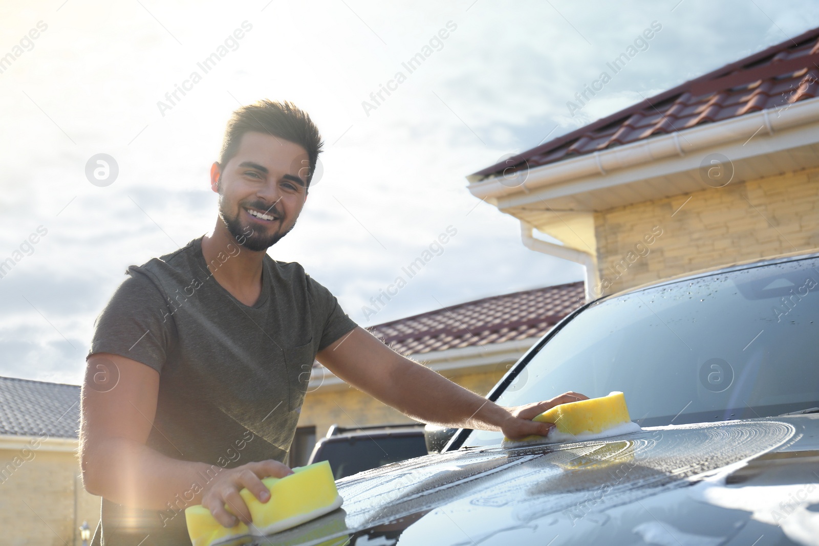 Photo of Young happy man washing car at backyard on sunny day