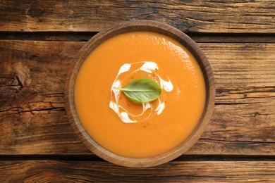 Photo of Tasty creamy pumpkin soup with basil in bowl on wooden table, top view