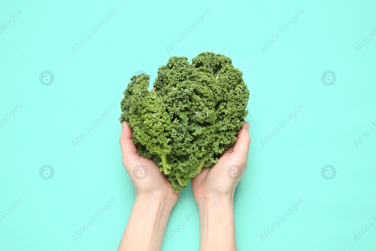 Photo of Woman holding fresh kale leaves on turquoise background, top view