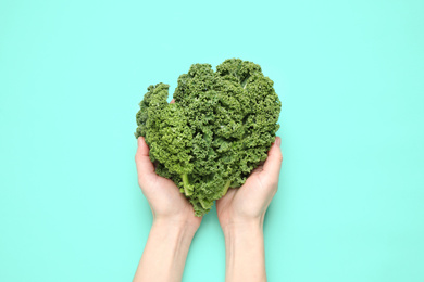 Photo of Woman holding fresh kale leaves on turquoise background, top view