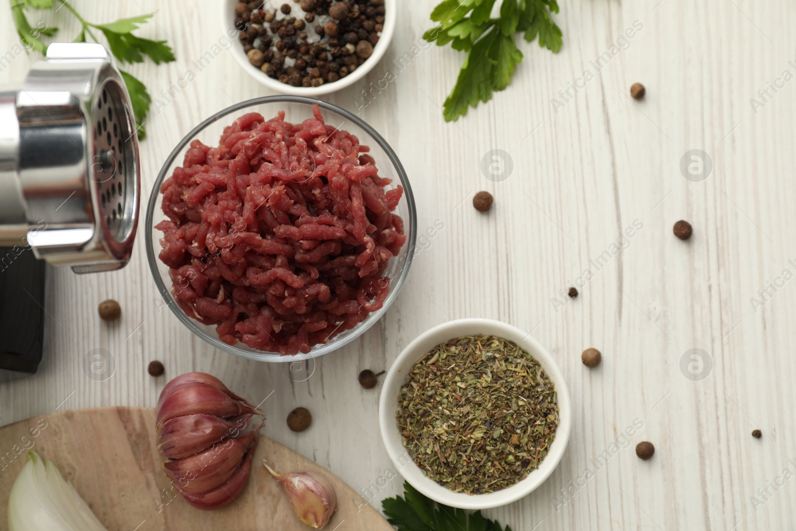 Photo of Meat grinder, beef mince, garlic, parsley and spices on white wooden table, flat lay