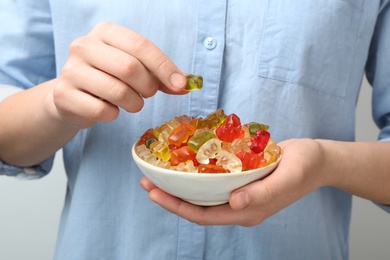 Woman holding bowl of colorful jelly bears on light background, closeup