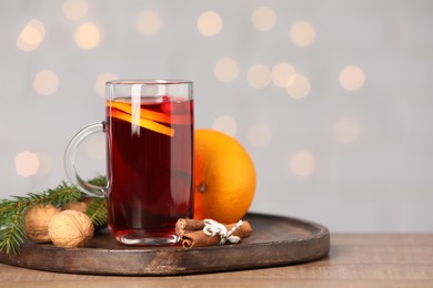 Aromatic mulled wine in glass cup on table against grey background with blurred lights, closeup. Space for text