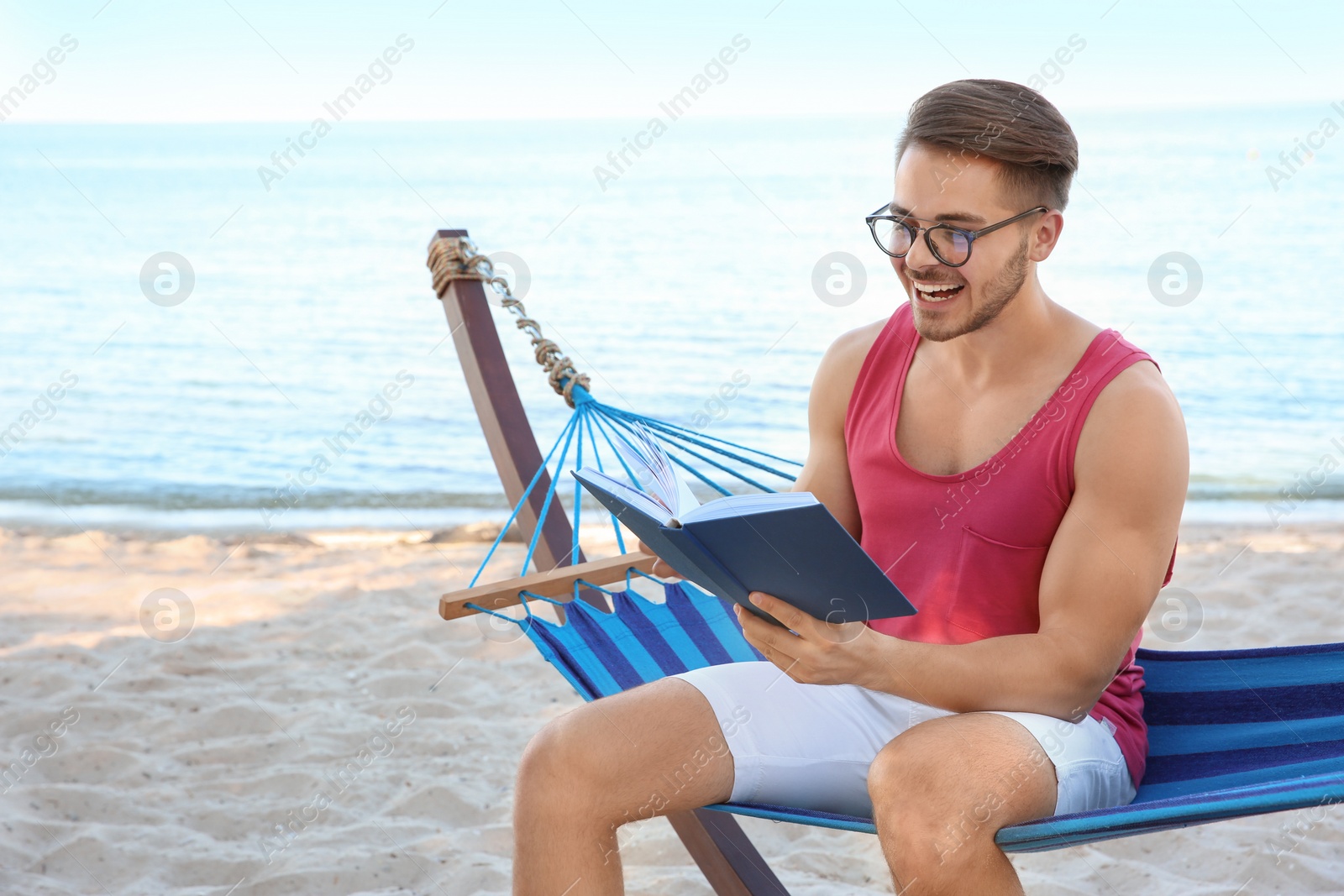 Photo of Young man reading book in hammock at seaside