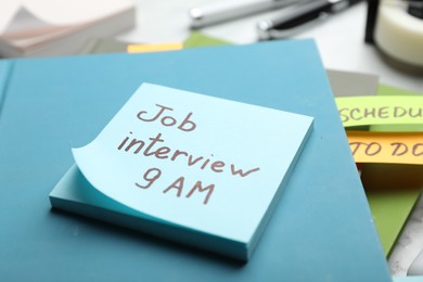 Photo of Reminder note about job interview and stationery on table, closeup