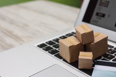 Photo of Internet shopping. Small cardboard boxes, credit card and laptop on light wooden table, closeup. Space for text