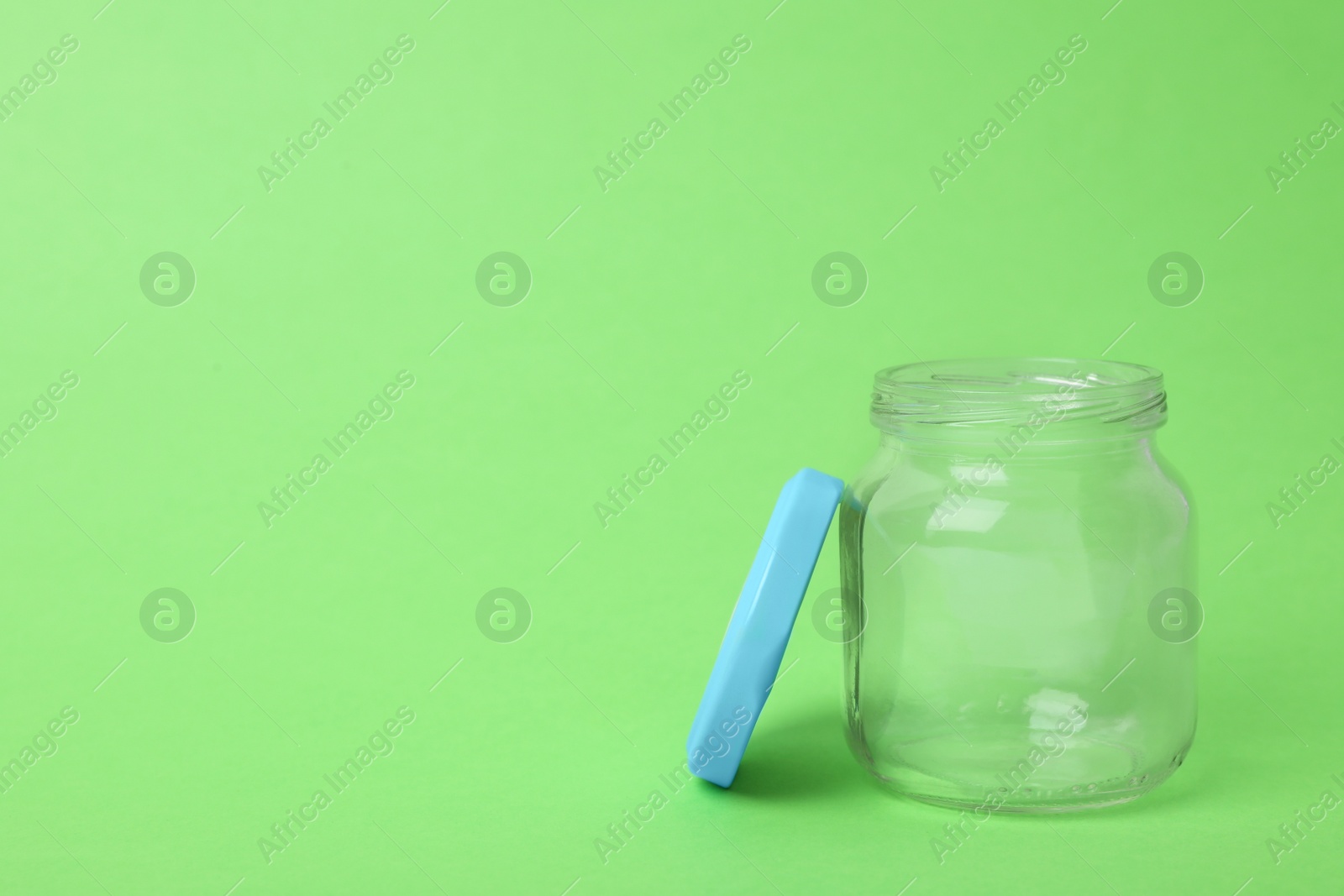 Photo of Open empty glass jar on light green background, space for text