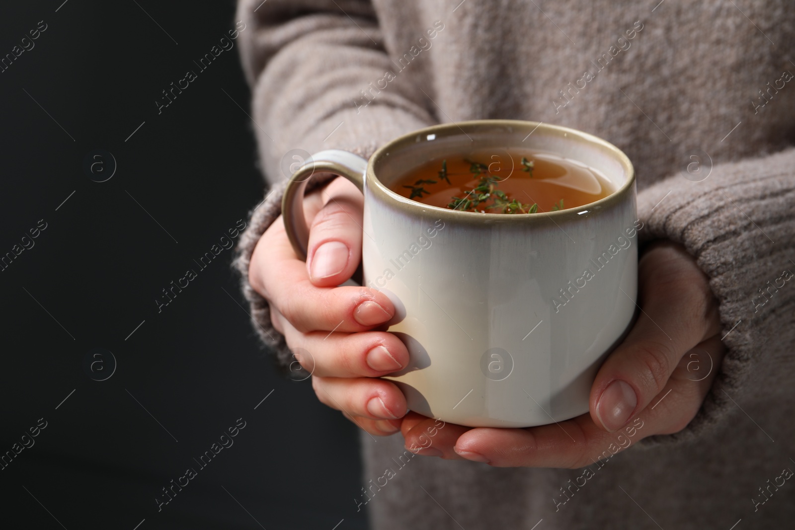 Photo of Woman holding cup of tasty herbal tea with thyme, closeup