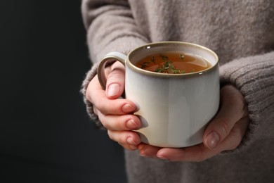 Photo of Woman holding cup of tasty herbal tea with thyme, closeup