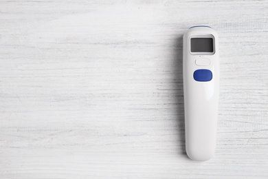 Photo of Modern non-contact infrared thermometer on white wooden background, top view. Space for text