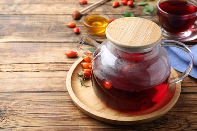 Photo of Teapot with aromatic rose hip tea and fresh berries on wooden table, space for text