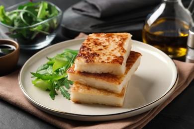 Photo of Delicious turnip cake with arugula served on black table