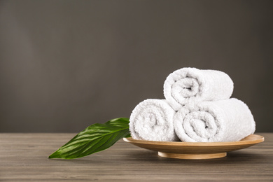 Photo of Fresh rolled towels and green leaf on grey wooden table