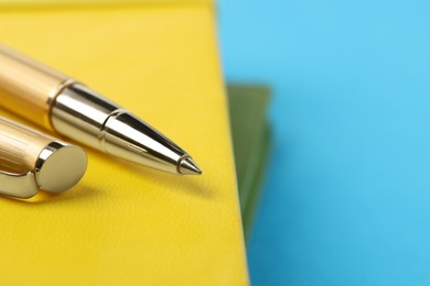 Photo of Ballpoint pen and yellow notebook on light blue background, closeup. Space for text