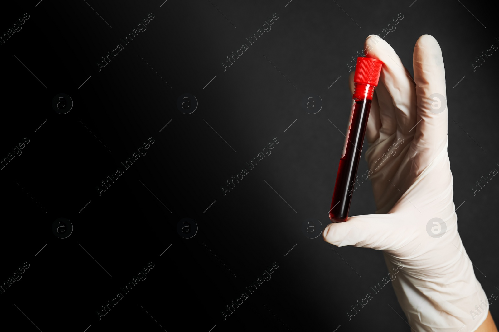 Photo of Scientist holding test tube of blood sample on black background, closeup with space for text. Virus research