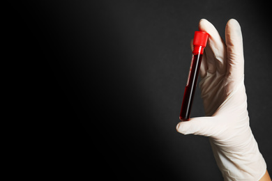 Photo of Scientist holding test tube of blood sample on black background, closeup with space for text. Virus research