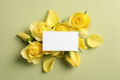 Beautiful yellow roses, petals and blank card on light olive background, flat lay. Space for text