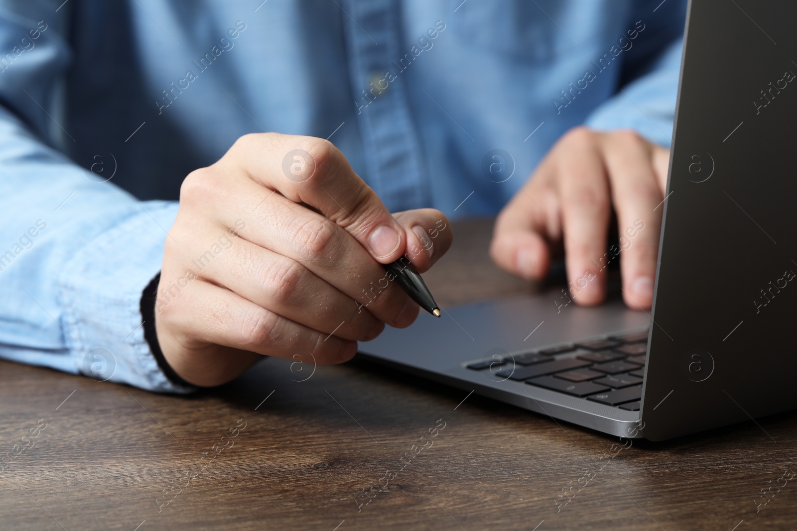 Photo of Man with pen and laptop at wooden table, closeup