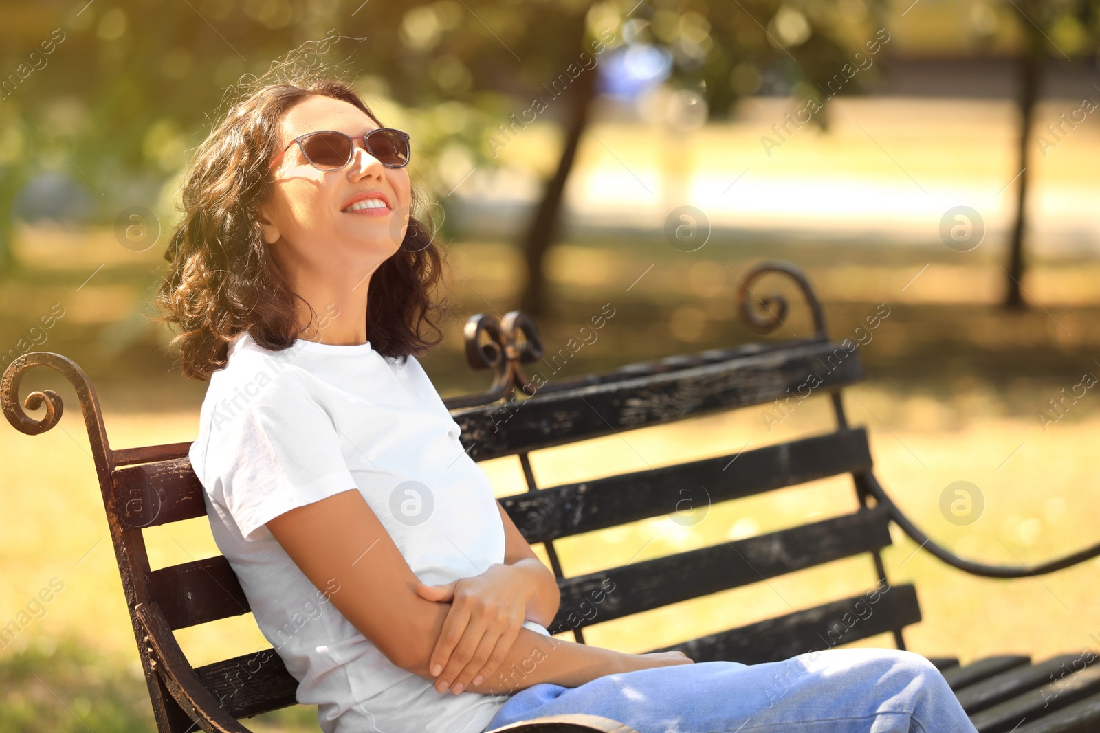Photo of Happy young woman sitting on bench in park