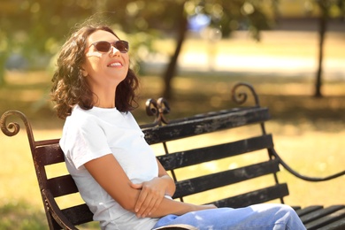 Photo of Happy young woman sitting on bench in park