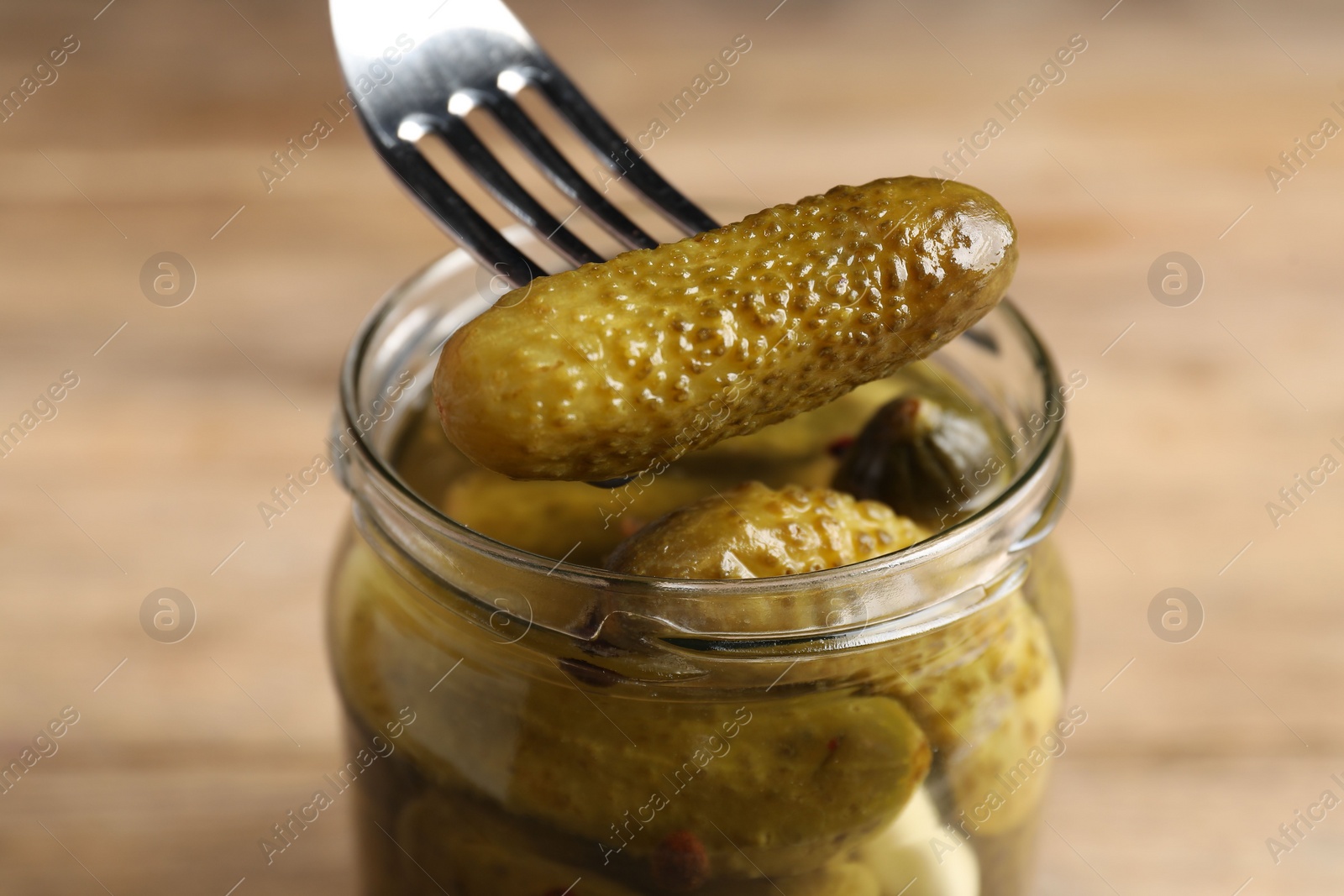 Photo of Eating tasty pickled cucumber from jar at table, closeup