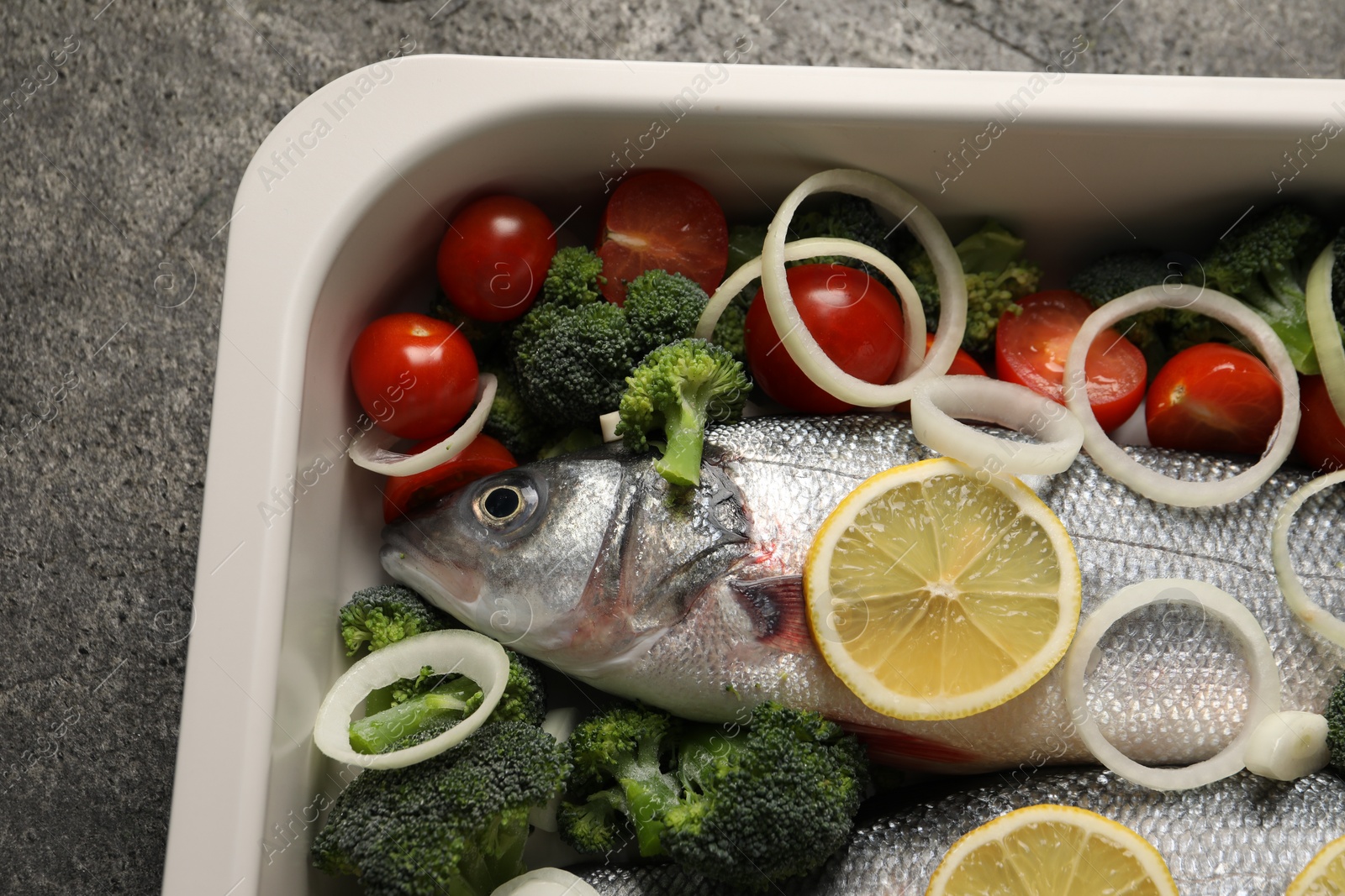 Photo of Raw fish with vegetables and lemon in baking dish on grey table. top view