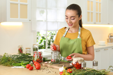 Woman putting tomatoes into pickling jar at table in kitchen