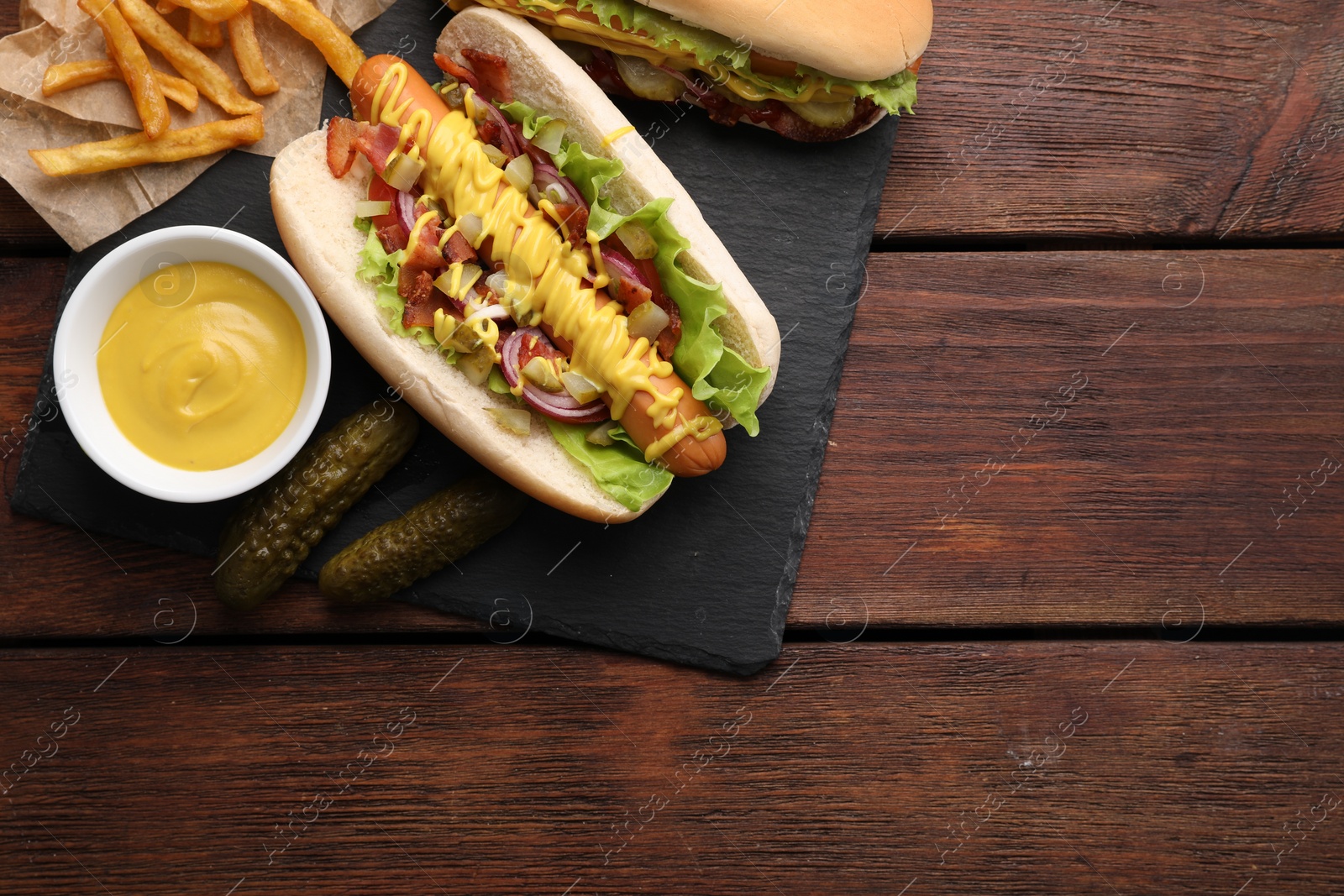 Photo of Delicious hot dogs with lettuce, onion and pickle served on wooden table, flat lay. Space for text