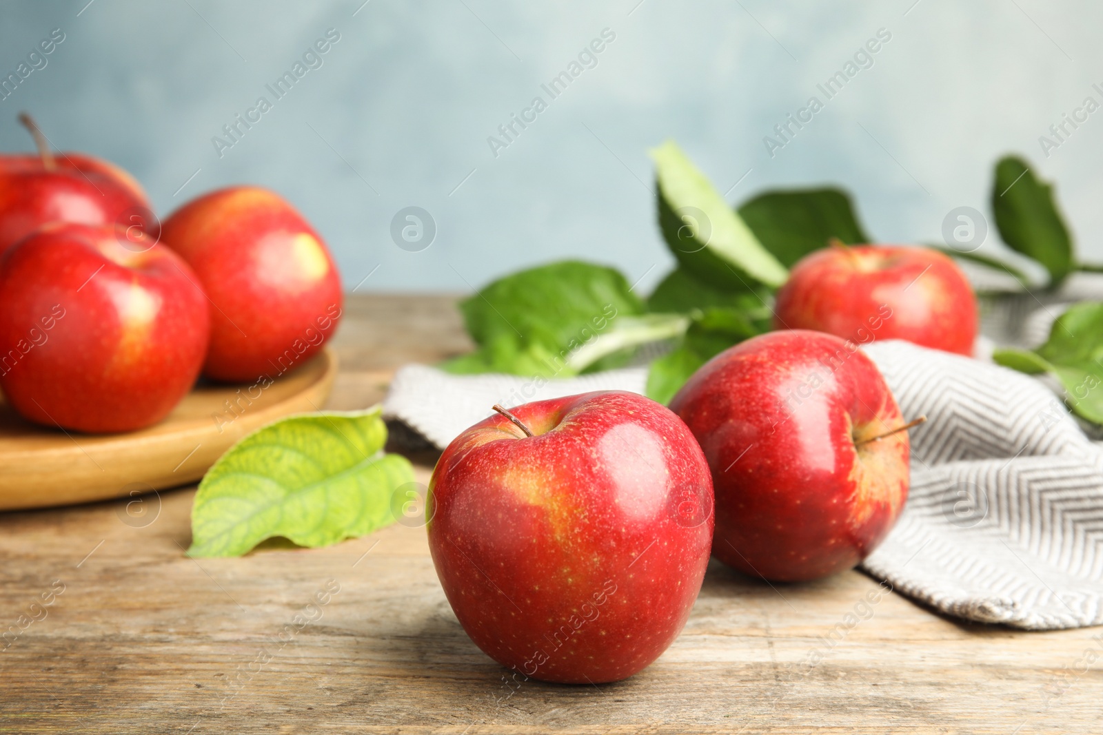 Photo of Ripe juicy red apples on wooden table against blue background. Space for text