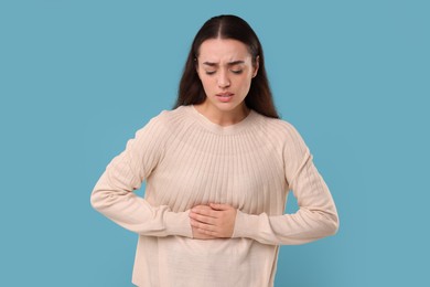 Photo of Woman suffering from abdominal pain on light blue background. Unhealthy stomach