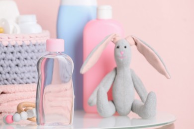 Baby cosmetic products, toys and accessories on white table against pink background