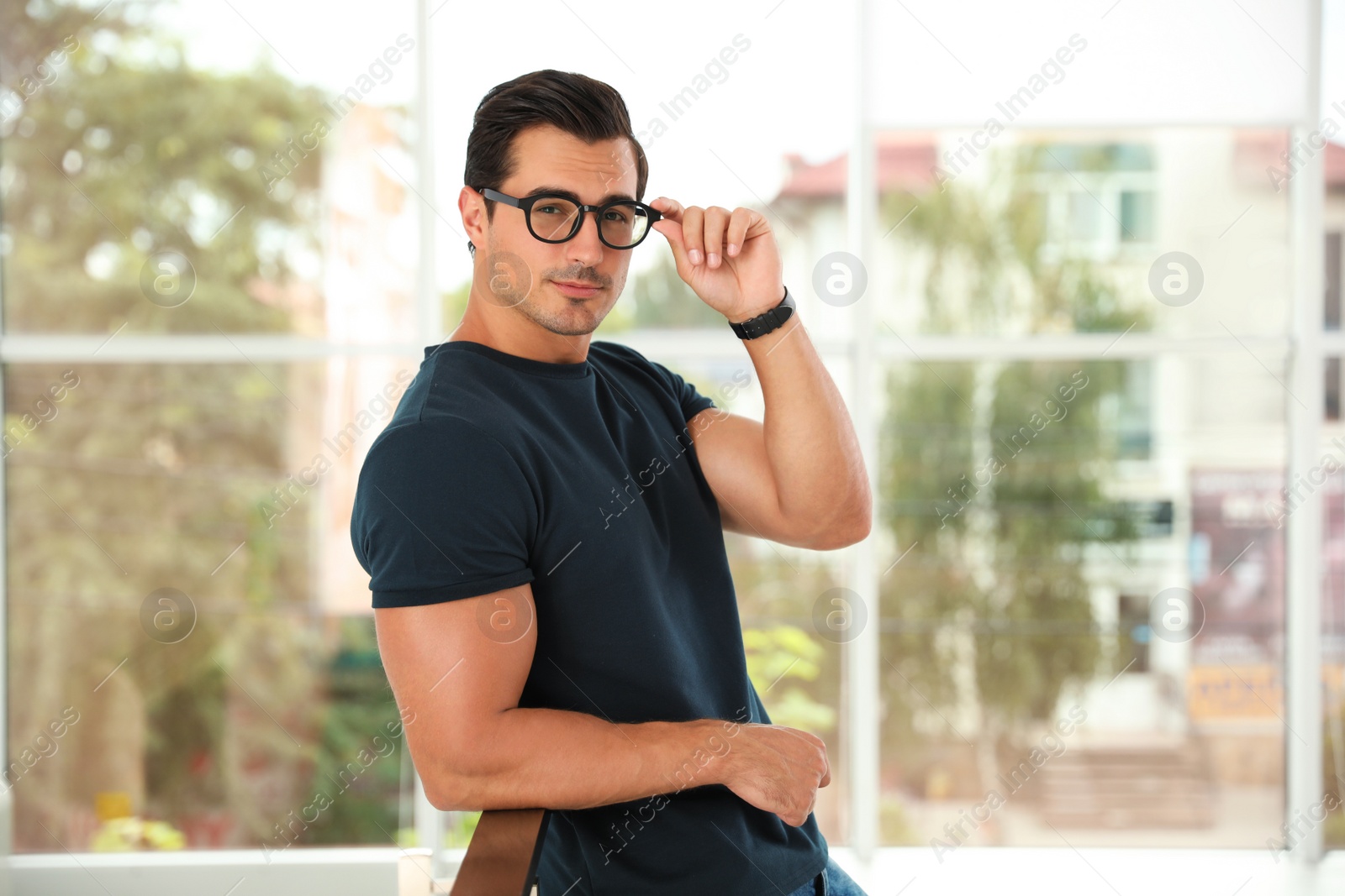 Photo of Portrait of handsome young man wearing glasses and leaning on railing indoors